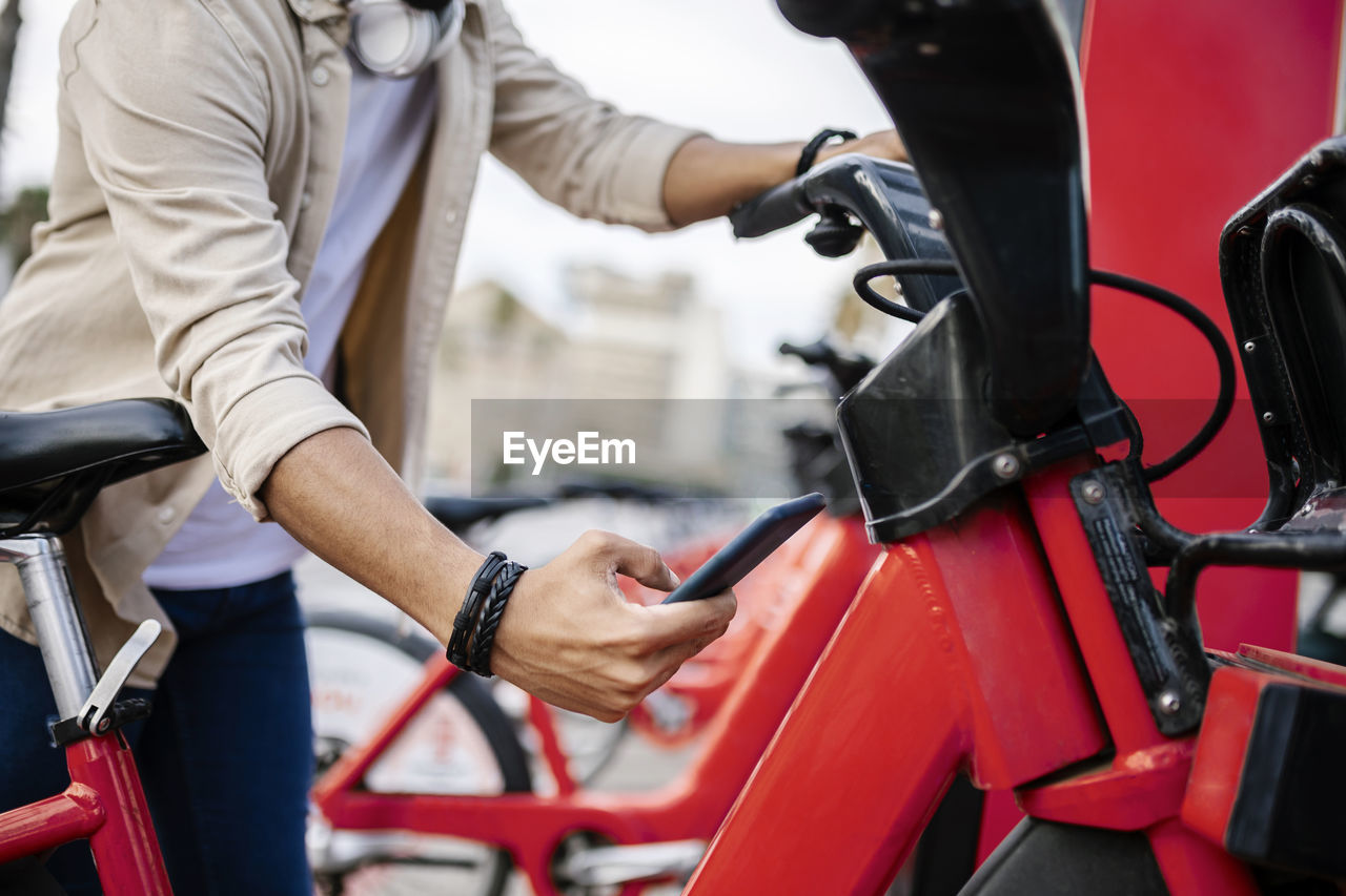 Man unlocking bicycle through smart phone at parking station