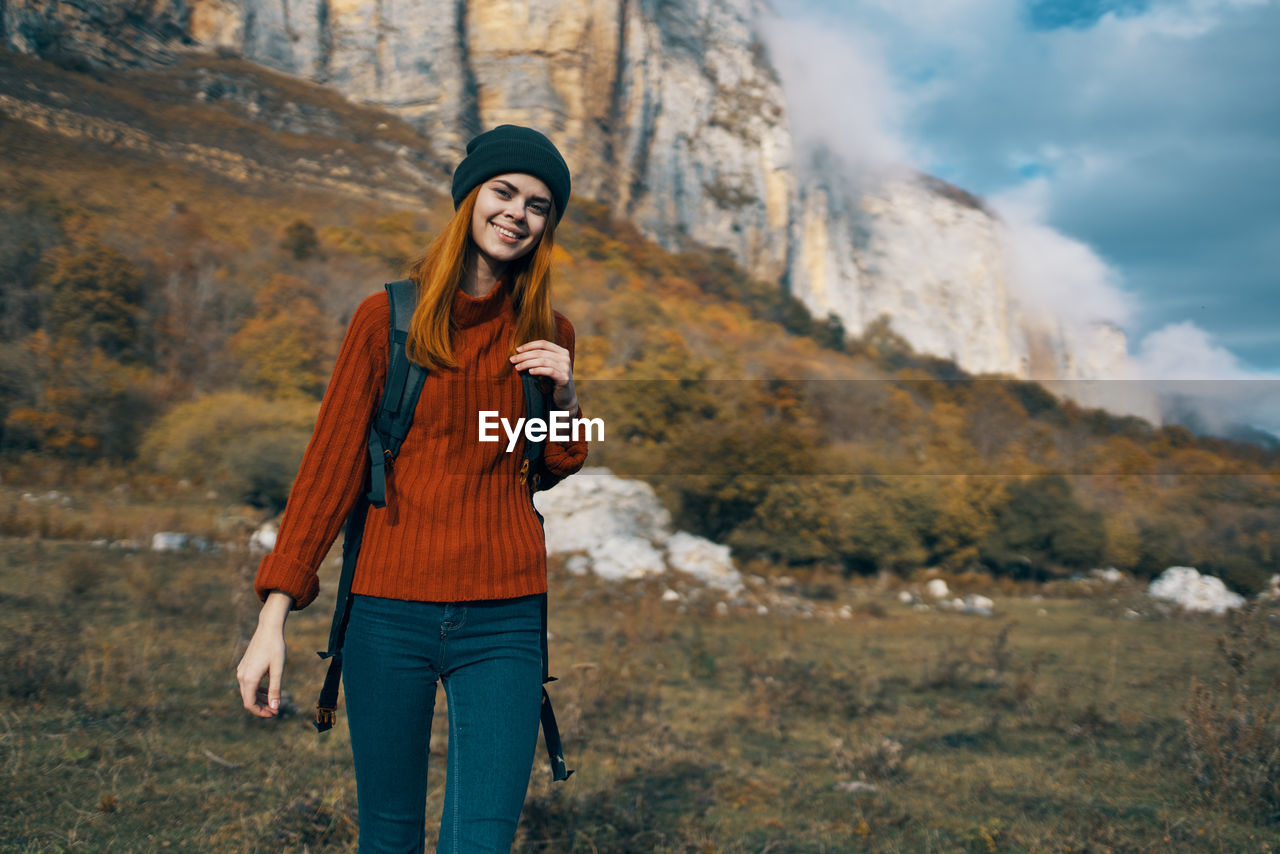 HAPPY YOUNG WOMAN STANDING ON MOUNTAIN