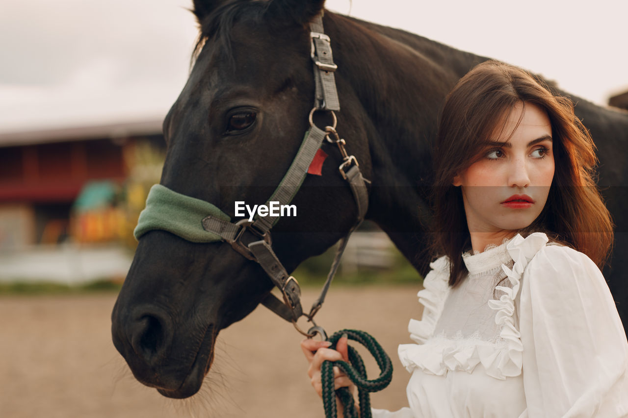 portrait of young woman with horse standing outdoors