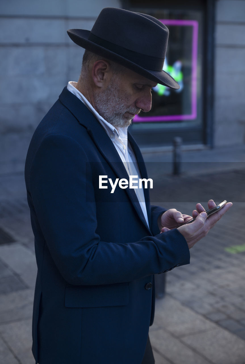 Adult man in suit and hat looking at mobile on street. madrid, spain