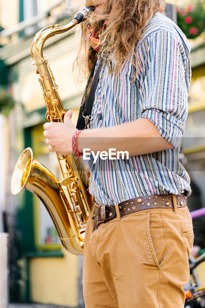 Hands of a young man with long hair playing saxophone in the street