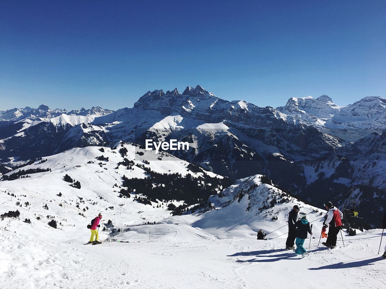 PEOPLE SKIING ON SNOWCAPPED MOUNTAIN AGAINST CLEAR SKY