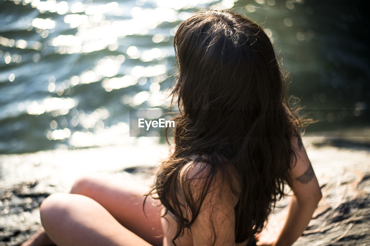 Young latina woman sitting by the ocean at golden hour in summertime