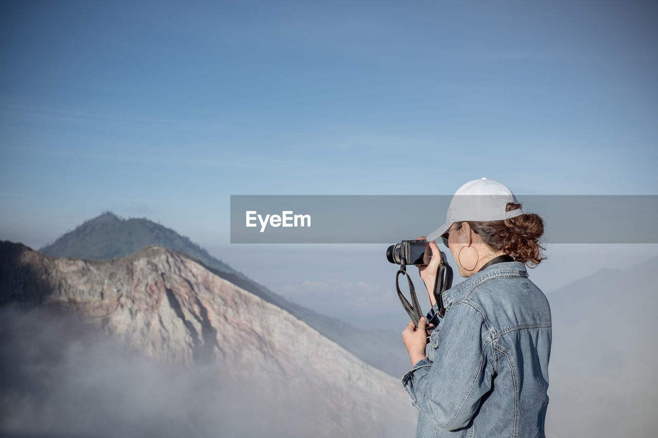 Woman photographing on mountain against sky