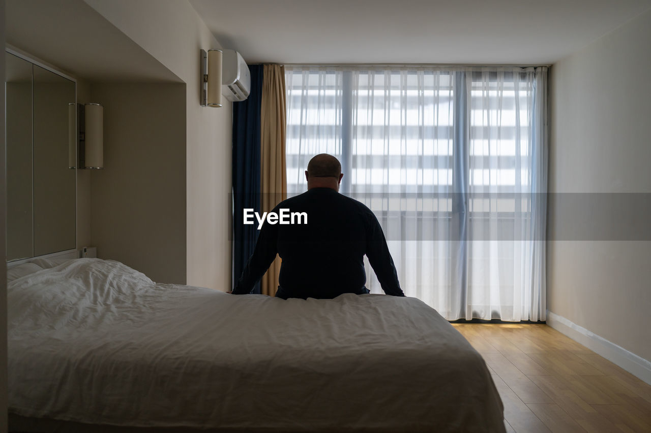 rear view of woman sitting on bed at home