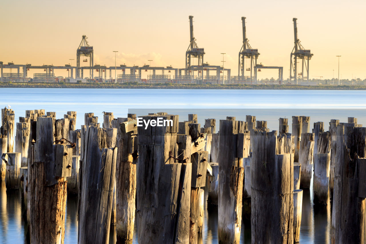 Princes pier view of wooden posts in sea against sky and cargo container cranes