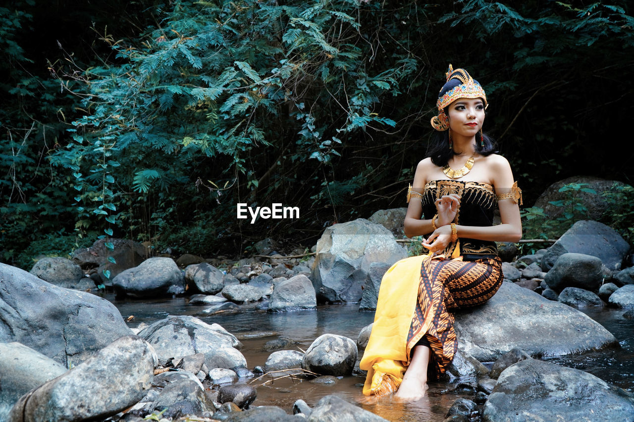 WOMAN SITTING ON ROCK IN FOREST