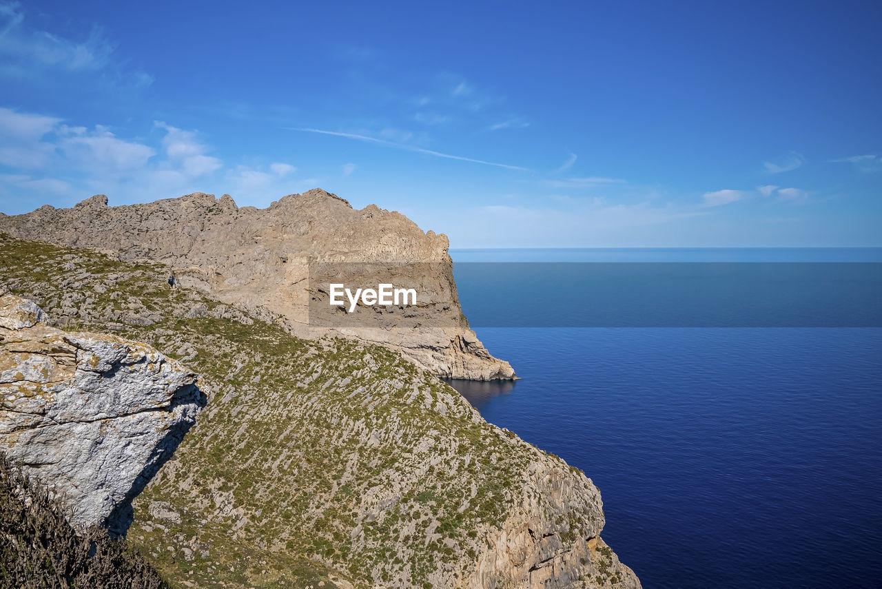 Scenic view of seascape by cliff against clear blue sky during sunny day