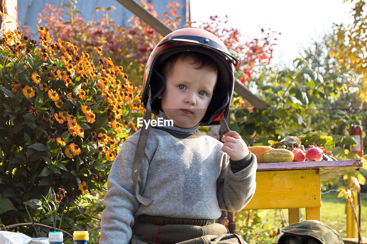 Portrait of cute boy wearing helmet sitting against plants