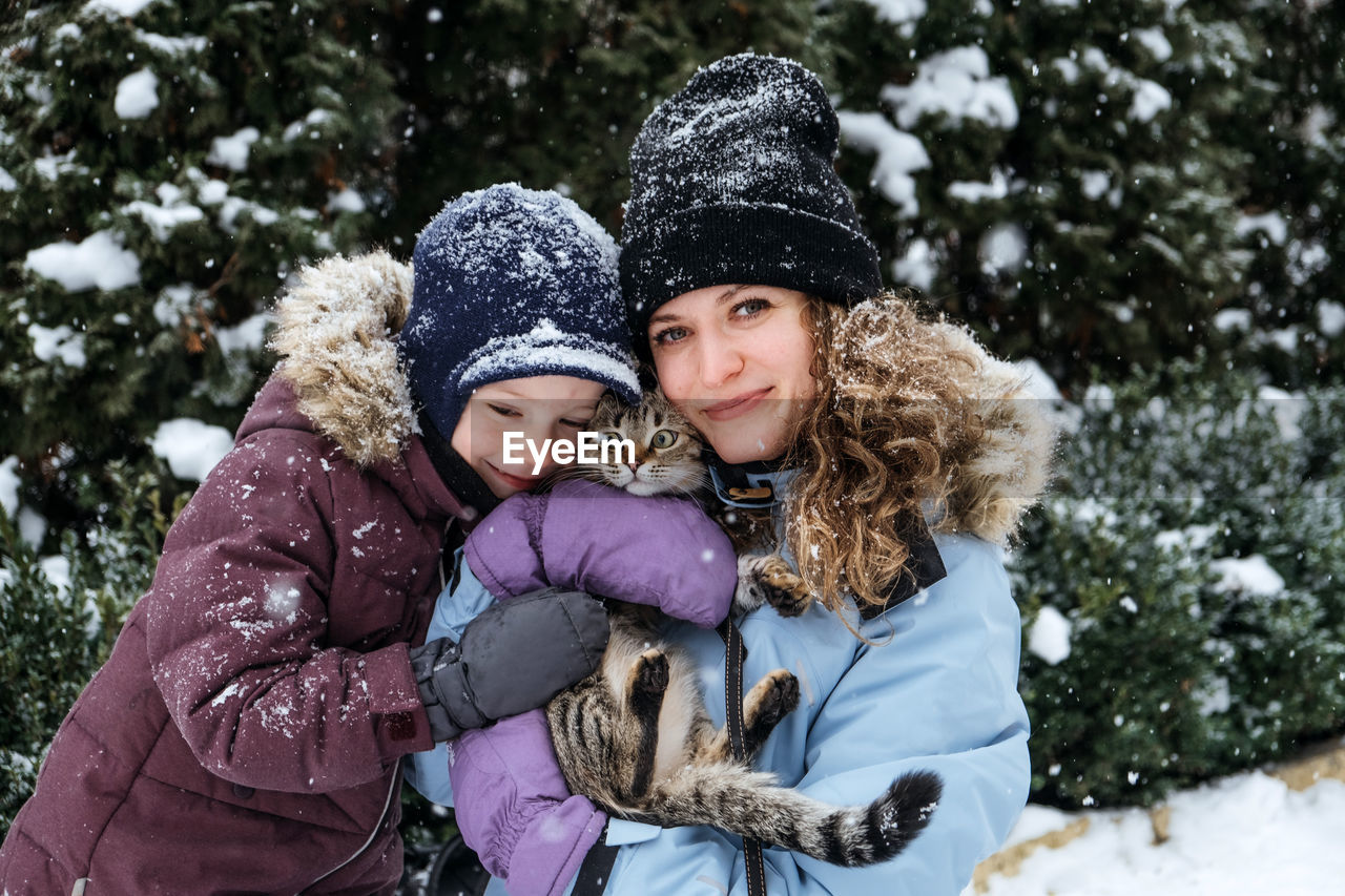 Portrait of happy family mother, son and cat in snowy winter park. outdoors portrait of mom and kid