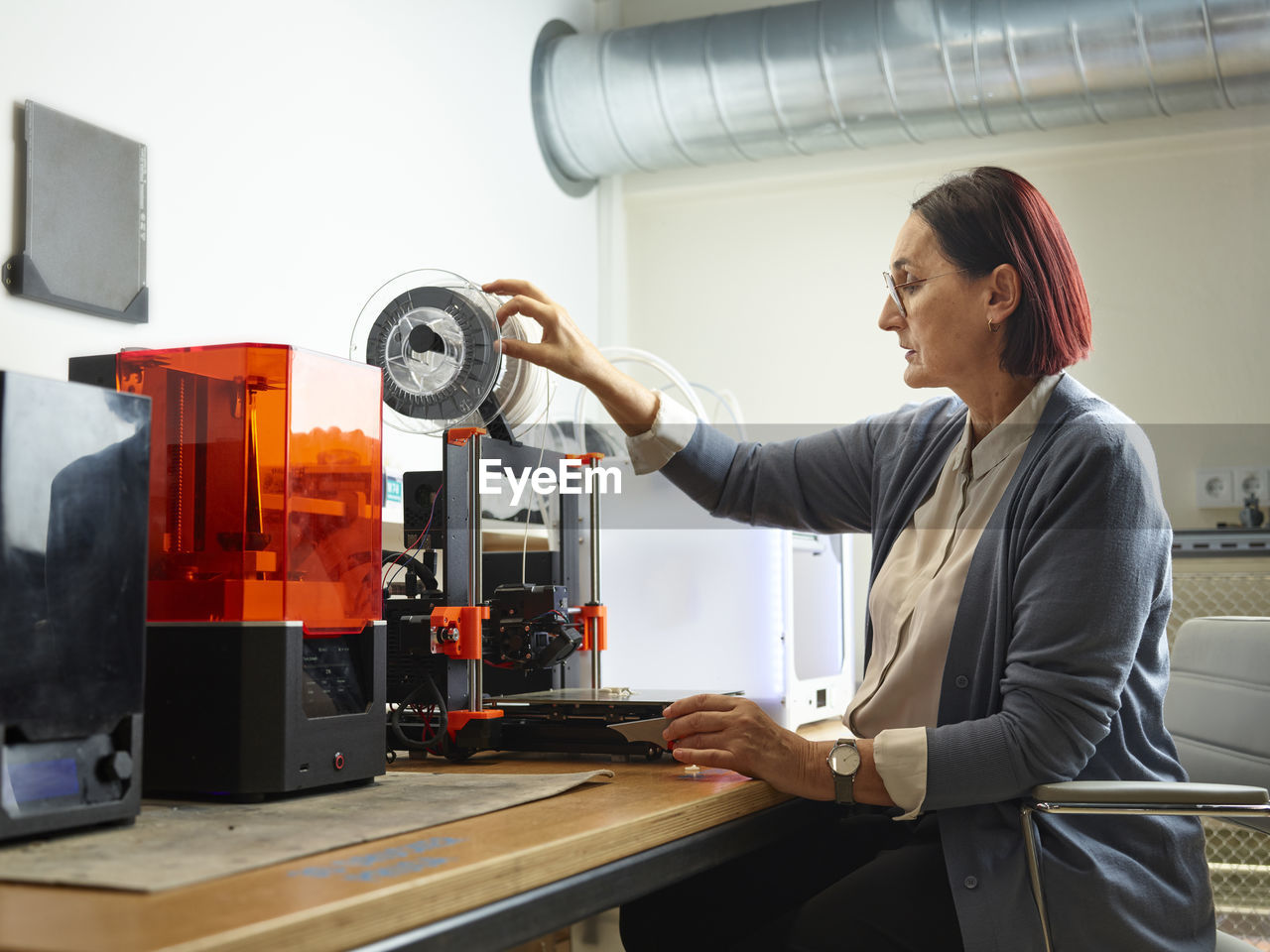 Engineer adjusting filament of 3d printer at workshop