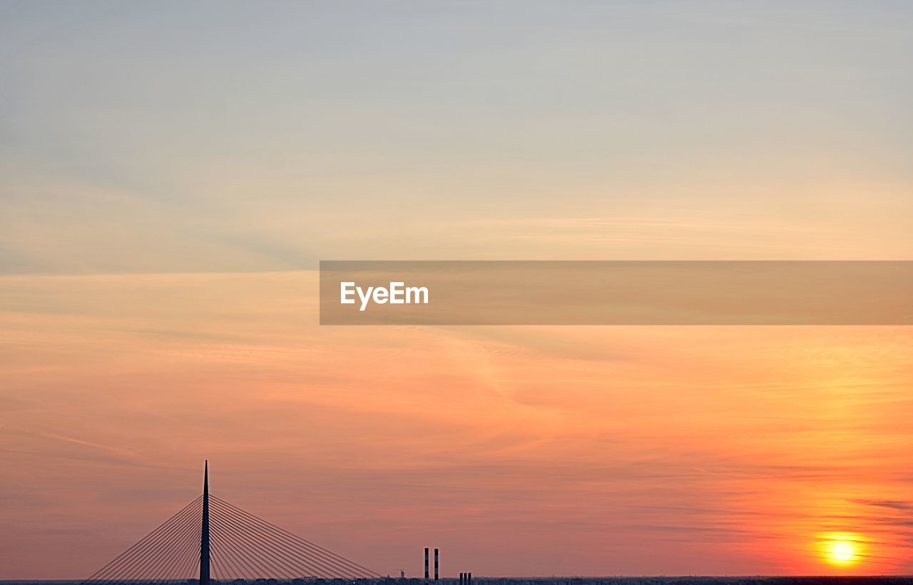 LOW ANGLE VIEW OF SUSPENSION BRIDGE AGAINST ORANGE SKY