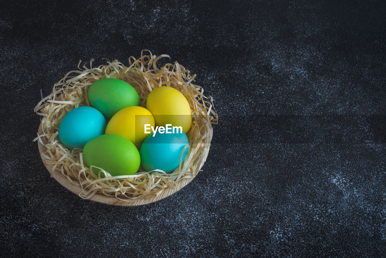 Colorful easter eggs in wooden plate decorated with decorative shavings on black background.