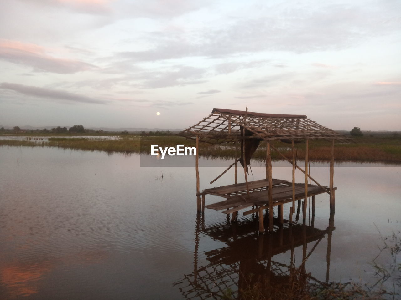water, reflection, sky, architecture, nature, cloud, lake, built structure, tranquility, stilt house, morning, beauty in nature, environment, scenics - nature, no people, shore, tranquil scene, outdoors, wood, landscape, pier, hut, travel destinations, wetland, building, dusk, beach, house, reservoir, building exterior, non-urban scene, travel, day, tourism