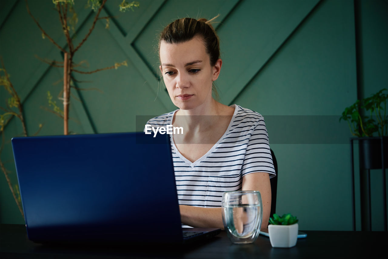 Caucasian woman sitting at table at home office and works with laptop. freelancer remotely working