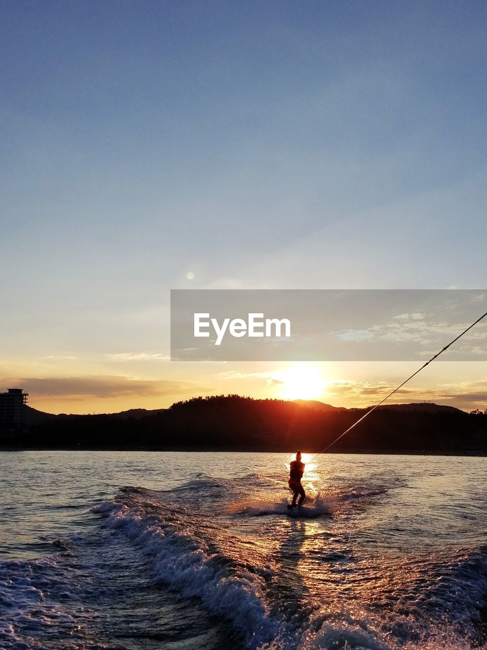 Silhouette woman surfing in sea against sky during sunset