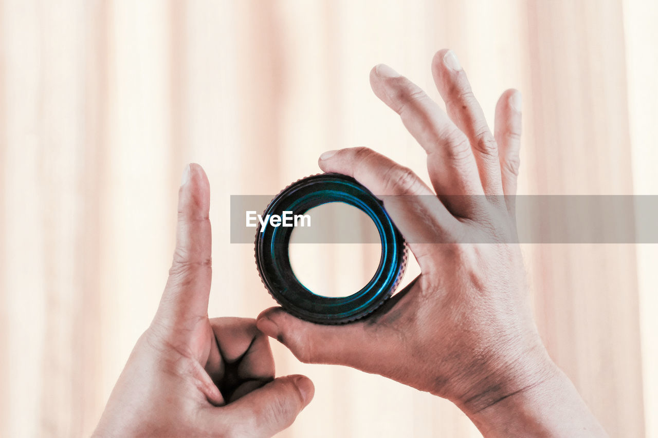 Cropped hands holding lens against curtain