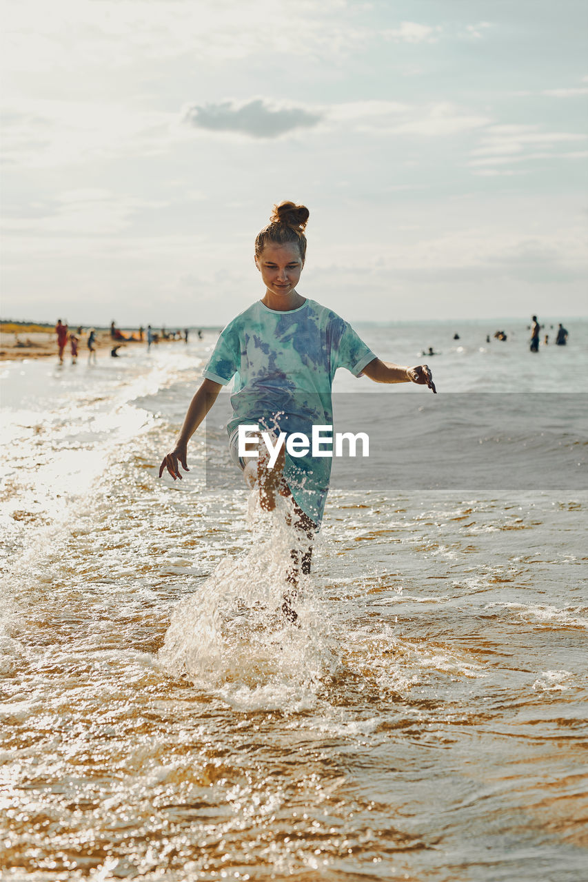 Girl splashing a water towards camera enjoying a free time over sea on a beach at sunset