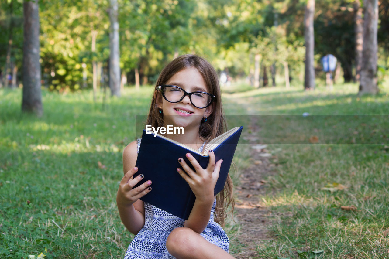 Portrait of cute girl reading book while sitting at park