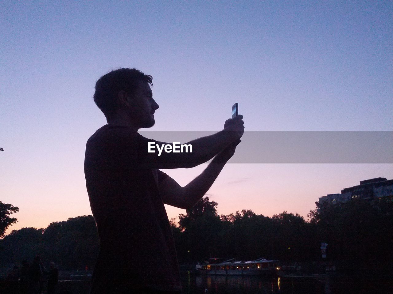 Side view of silhouette man with camera phone against clear sky