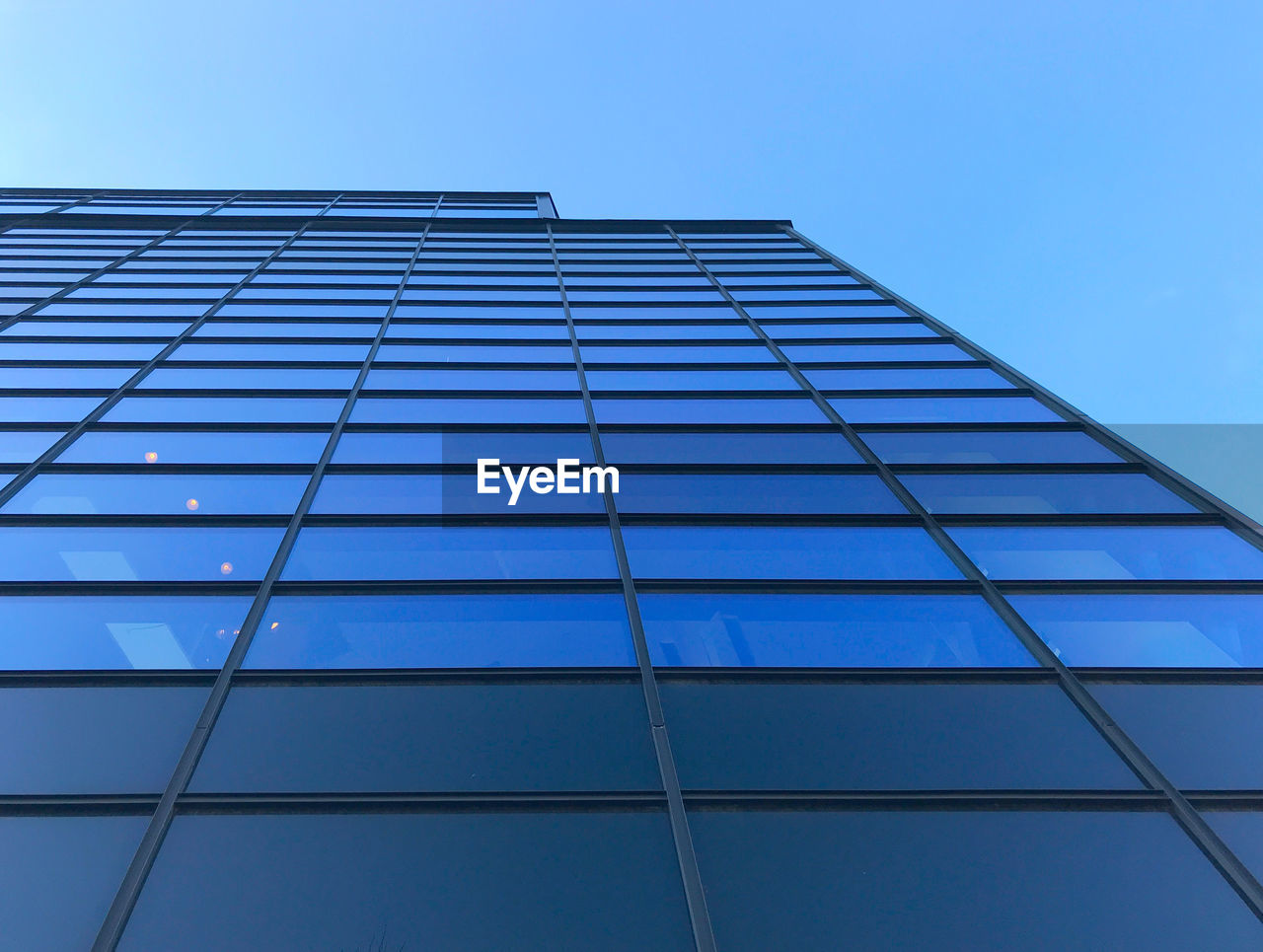 LOW ANGLE VIEW OF GLASS BUILDING AGAINST BLUE SKY