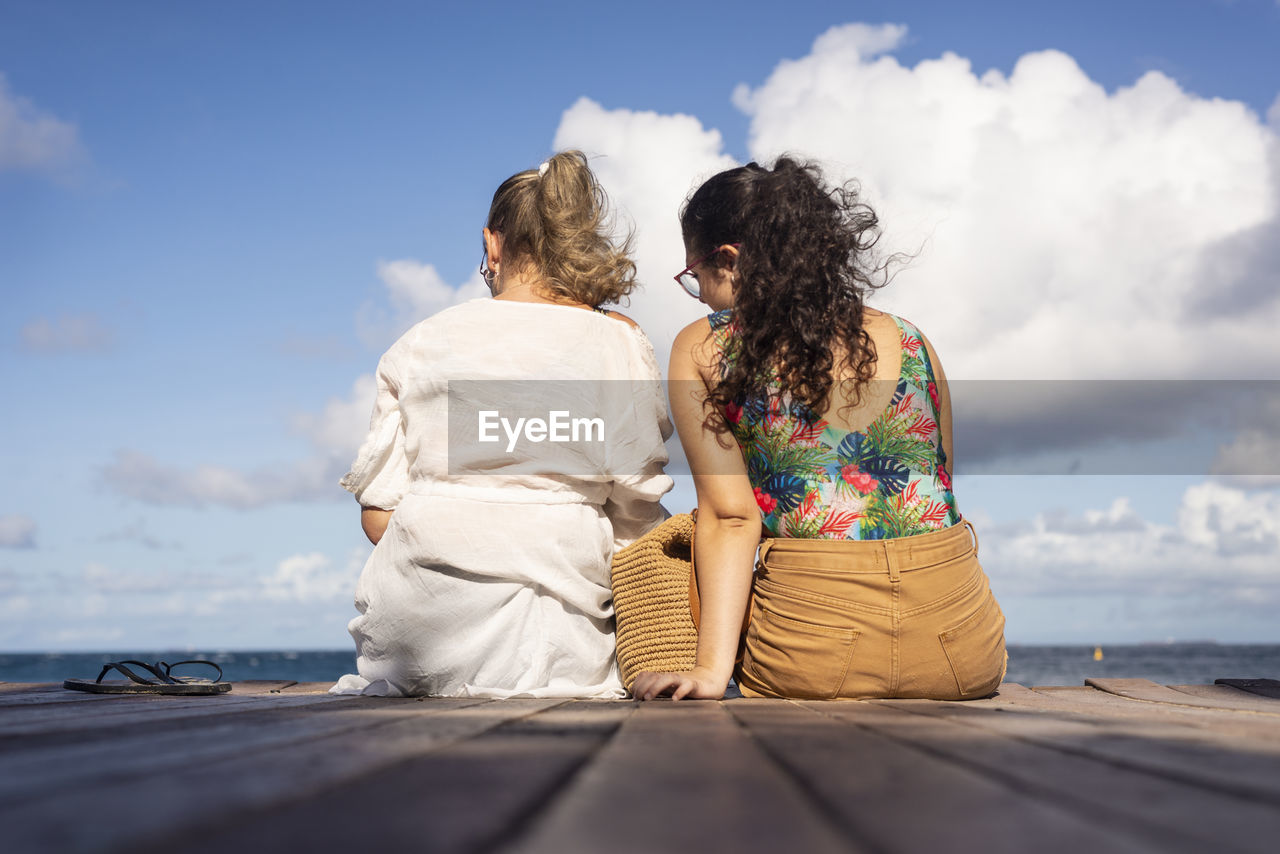 Mother and daughter sitting on the pier of the port of barra facing the sea. 