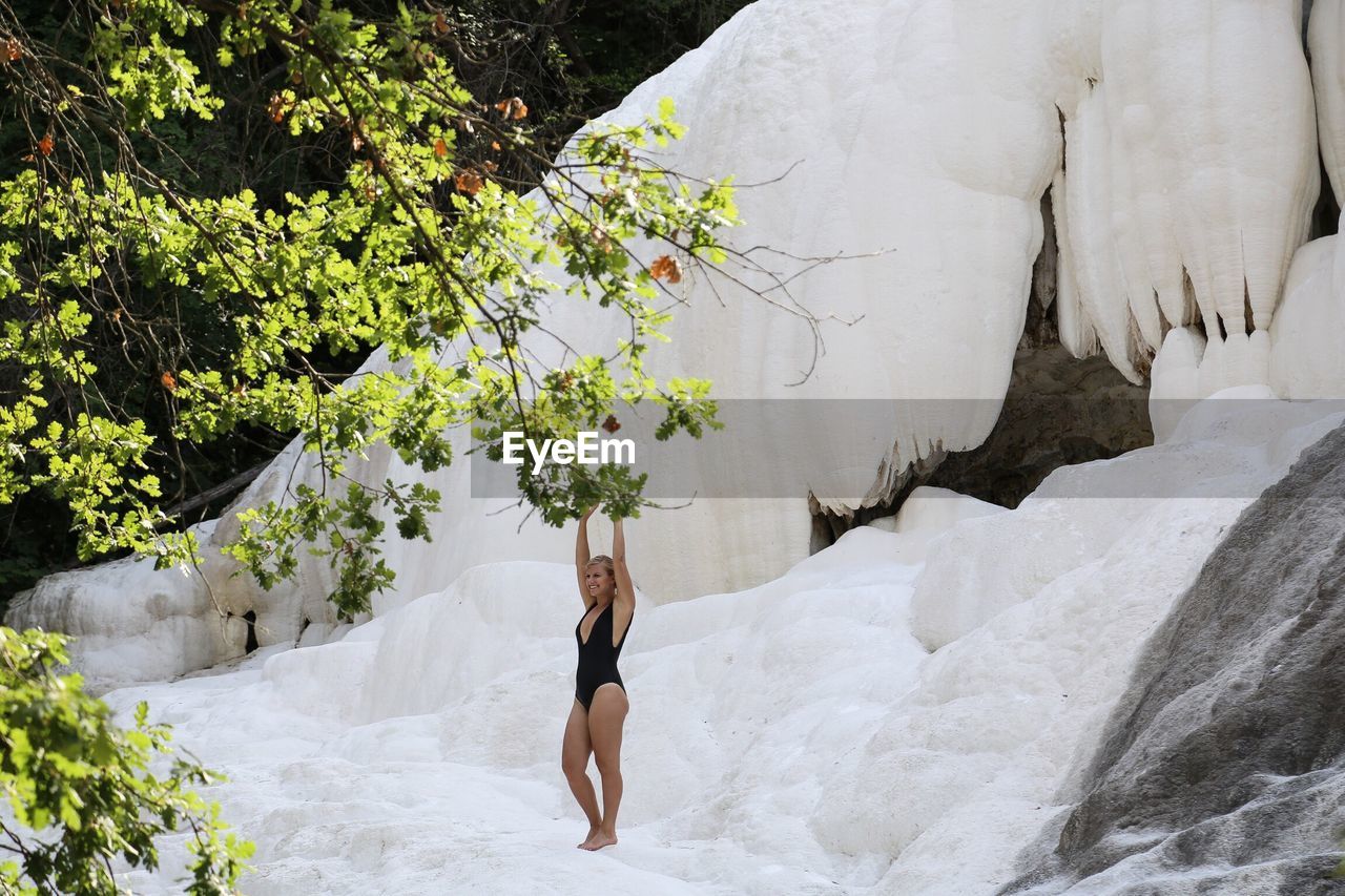 Woman standing on snow covered rock by tree