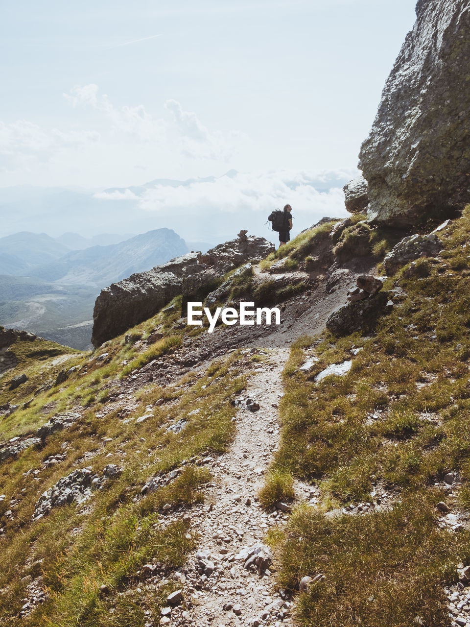 Young male with backpack looks up to his goal in climbing, the summit