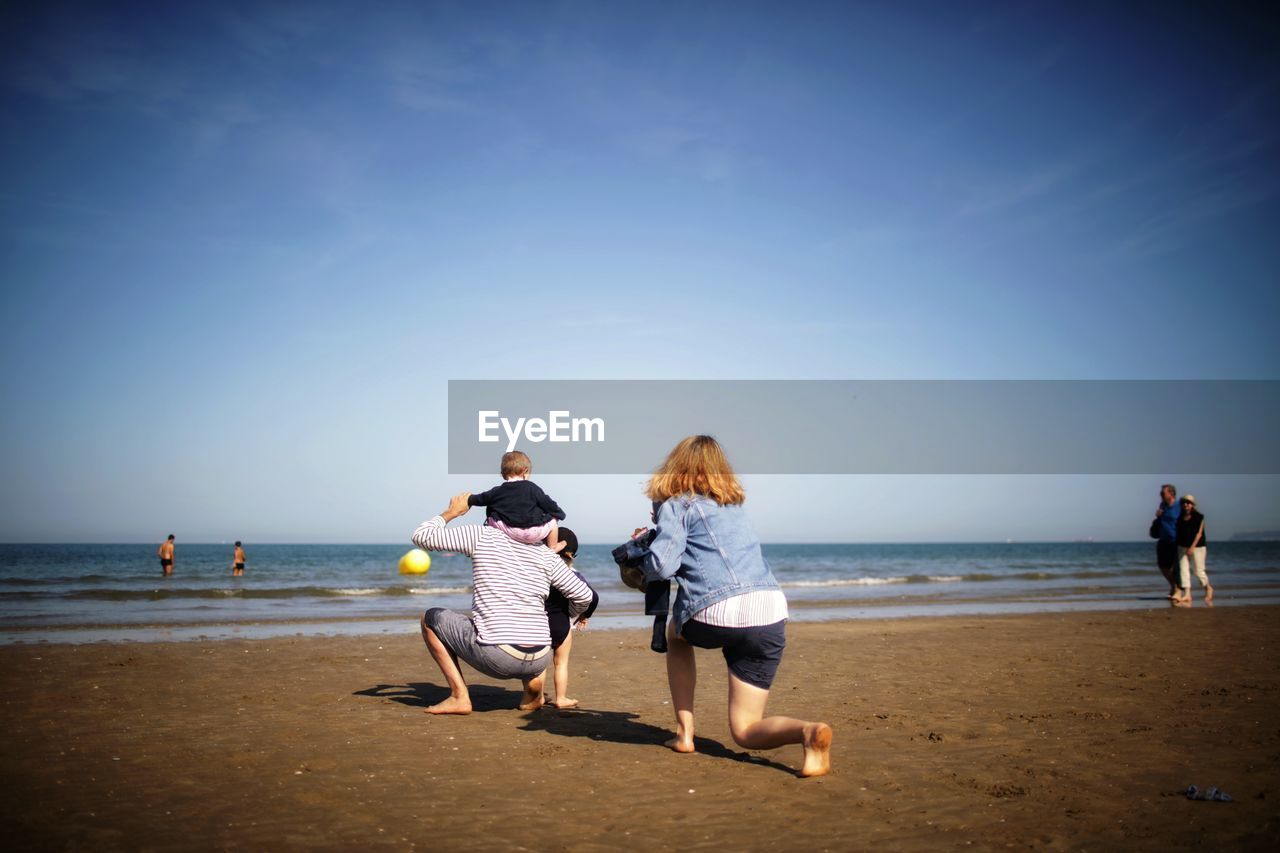 REAR VIEW OF PEOPLE ON BEACH AGAINST SEA