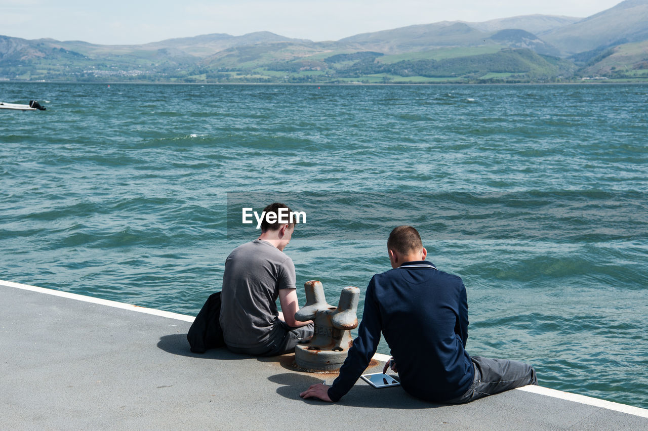 Rear view of friends sitting on pier over sea