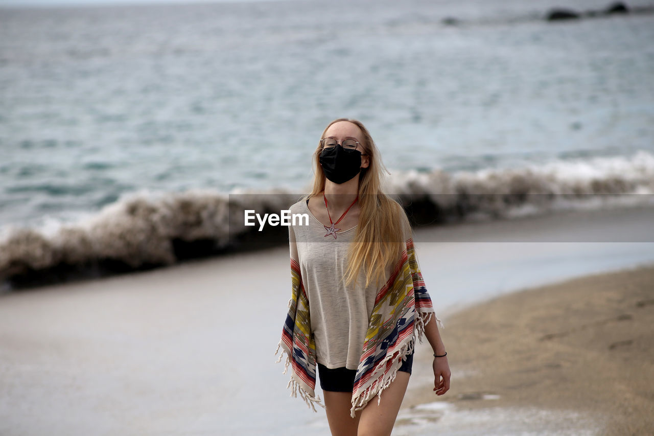 Portrait of woman wearing mask walking at beach
