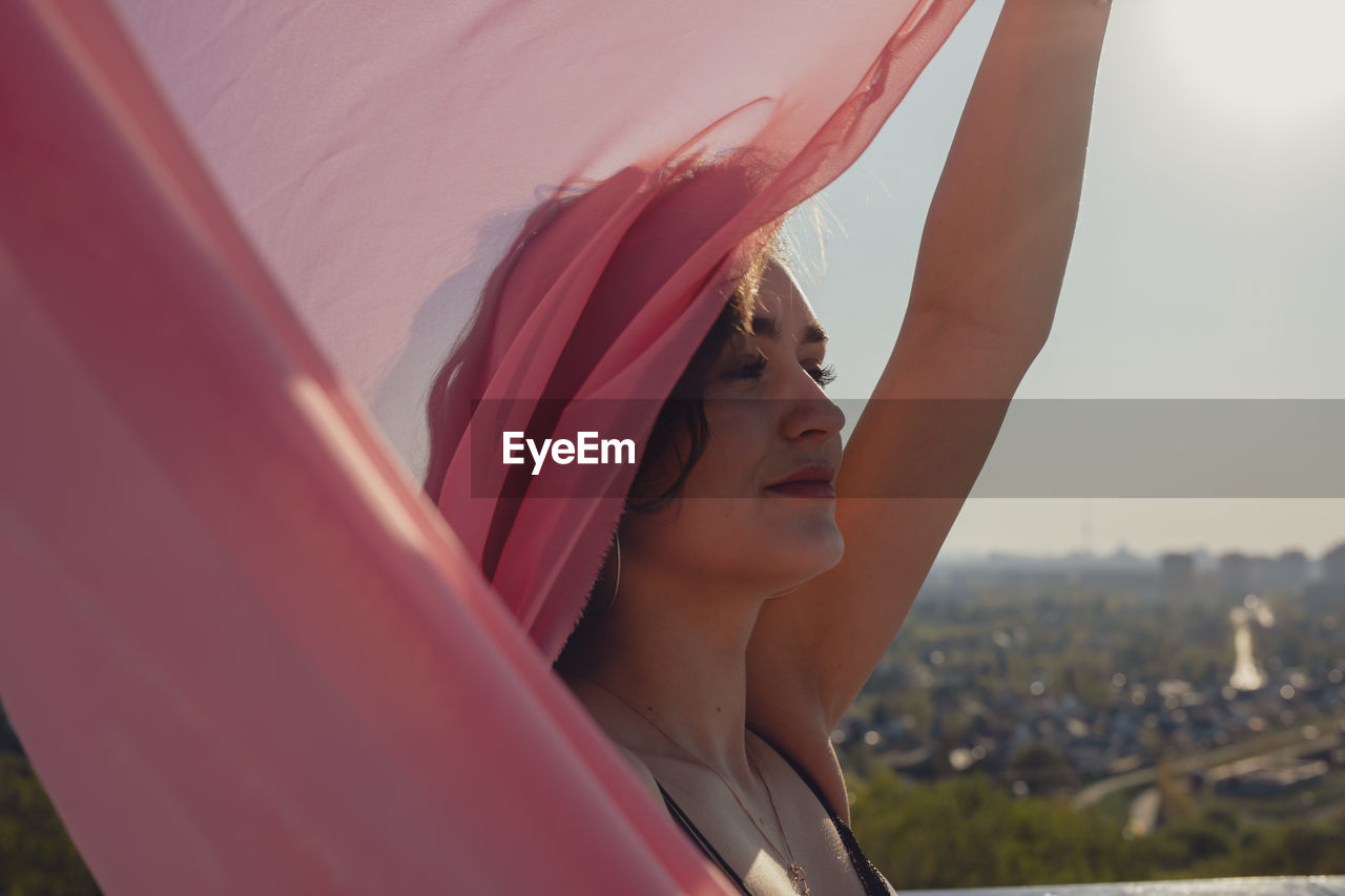 Young woman with pink scarf standing against sky during sunset