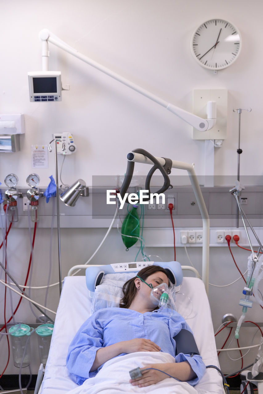 High angle view of female patient wearing oxygen mask while resting on bed in hospital