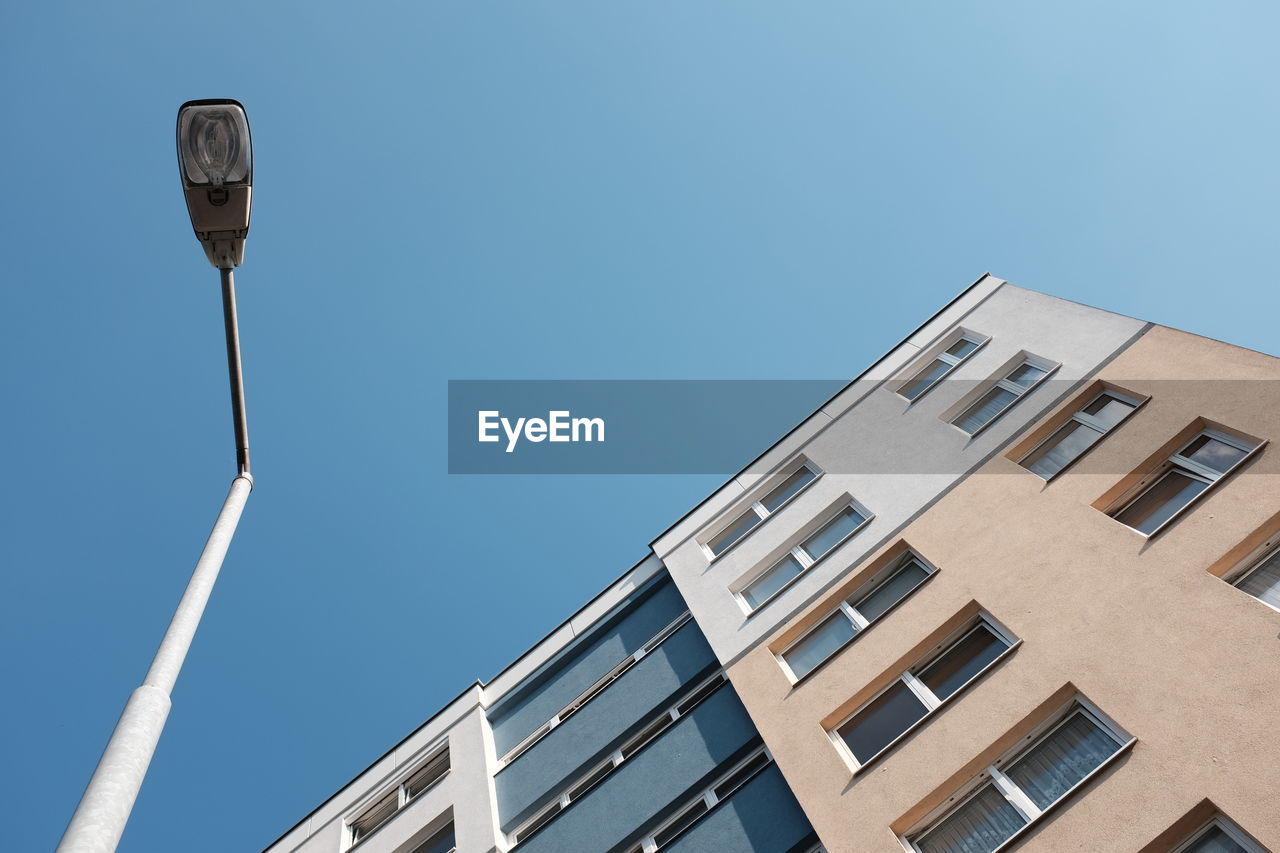 Low angle view of street light by building against clear blue sky