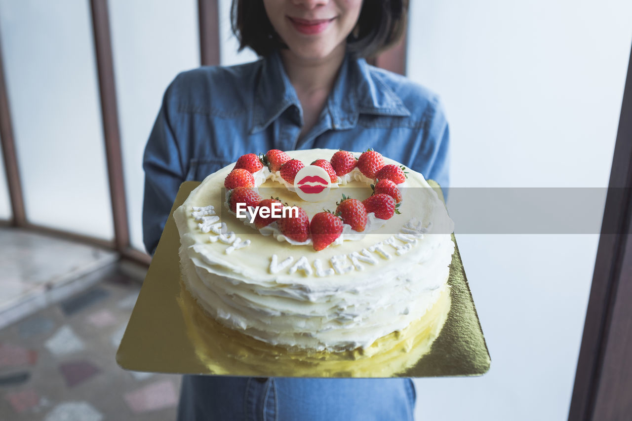 Midsection of young woman holding valentine cake at home