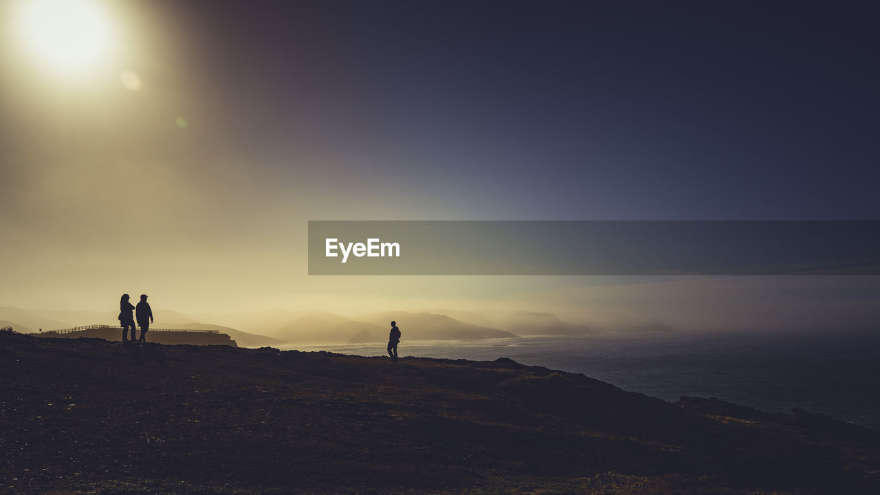 Silhouette people standing on mountain by sea against sky during sunset