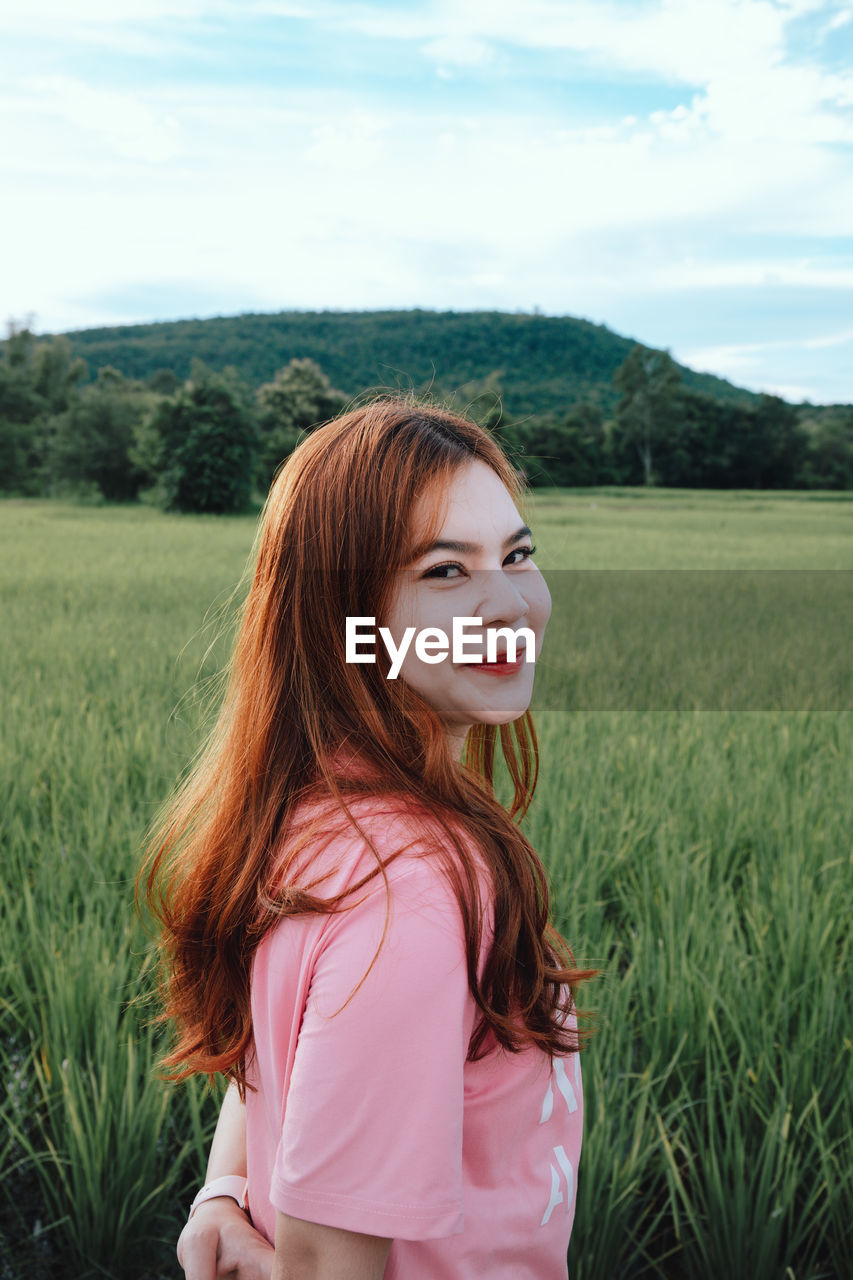 Portrait of young woman standing on field against sky