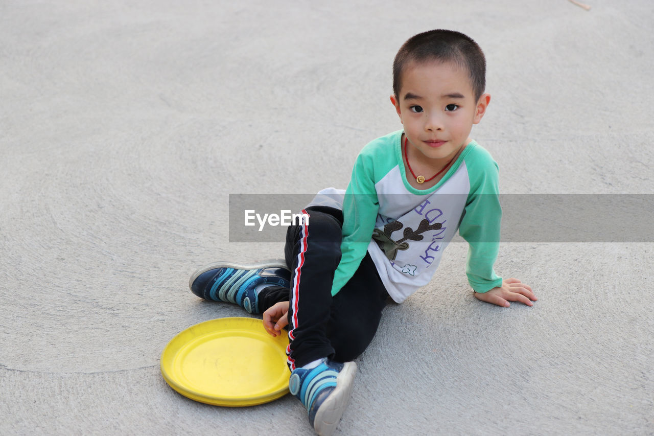 Portrait of boy sitting with plastic disc on footpath at park