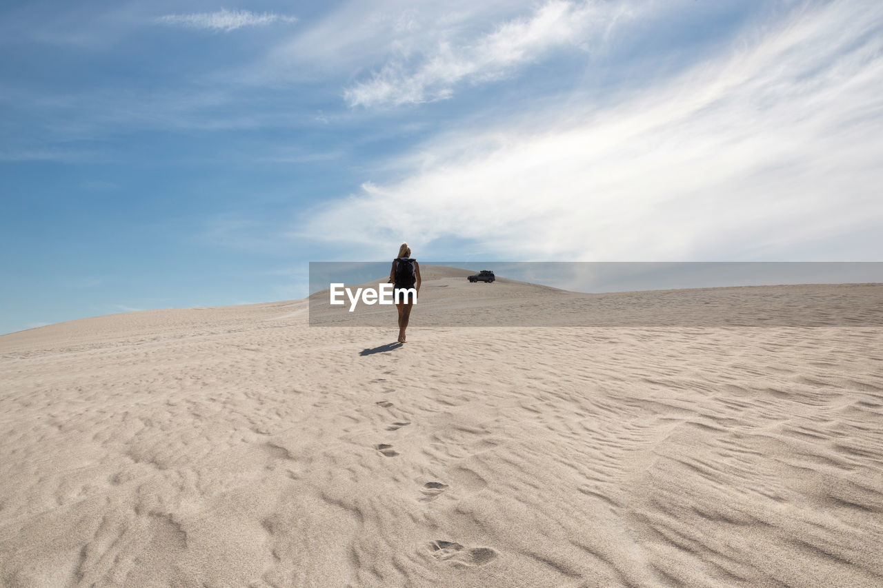 Rear view of woman walking on sand dune against sky