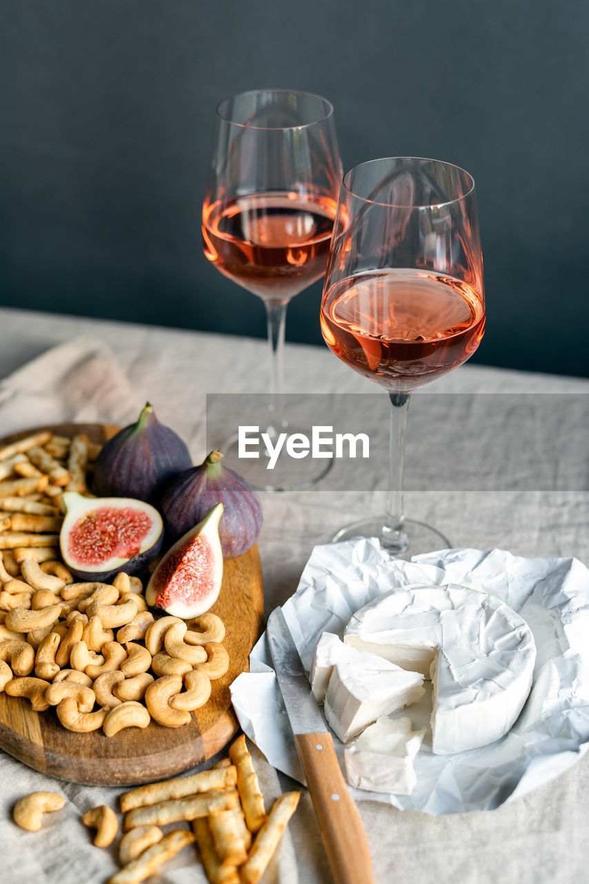 Rose wine with ripe figs, camembert cheese and cashews on a table indoors.