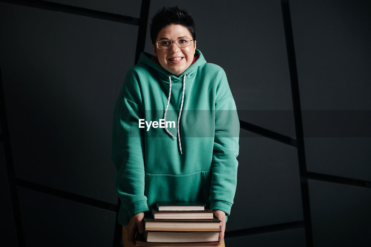 PORTRAIT OF A SMILING YOUNG MAN SITTING ON STACK OF BOOKS