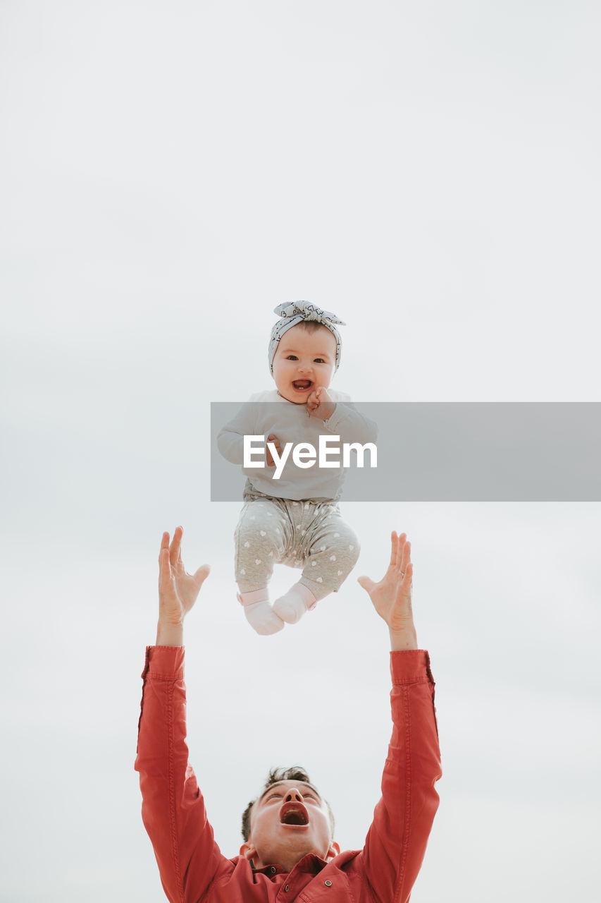 PORTRAIT OF HAPPY BOY WITH ARMS RAISED AGAINST SKY