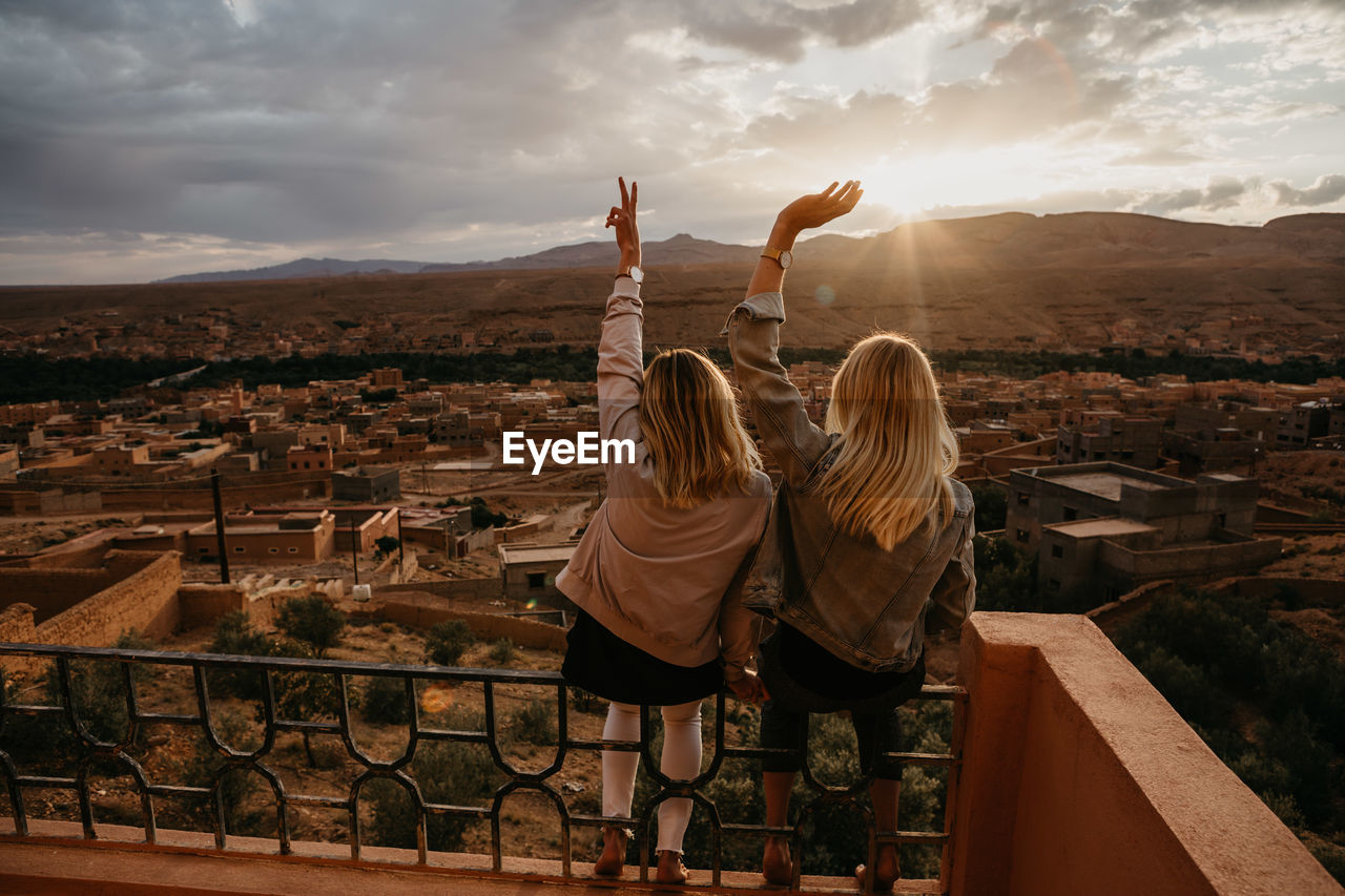 REAR VIEW OF WOMEN STANDING ON CITYSCAPE AGAINST SKY