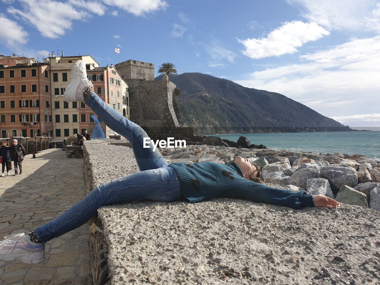 Side view of woman lying on wall by sea against sky