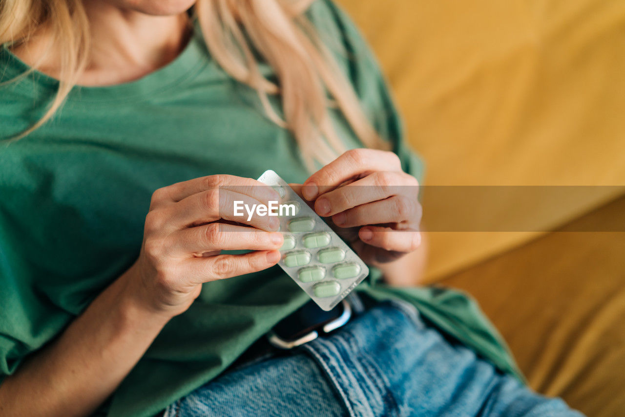 An unrecognizable woman takes one pill out of a pack of pills.