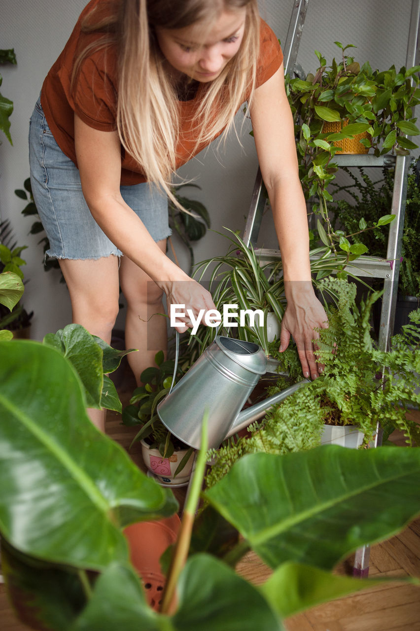 Woman watering plants on metal stepladder from watering can