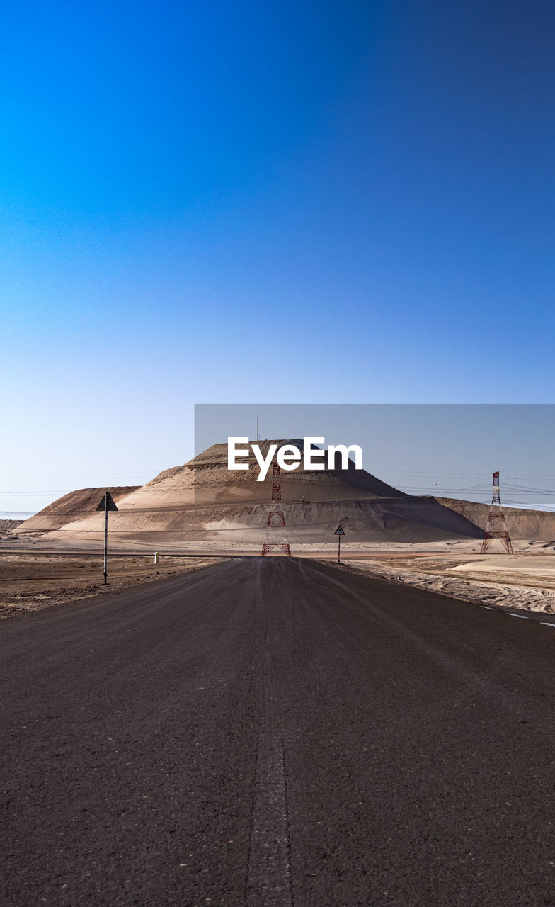 Road leading towards mountain against clear blue sky