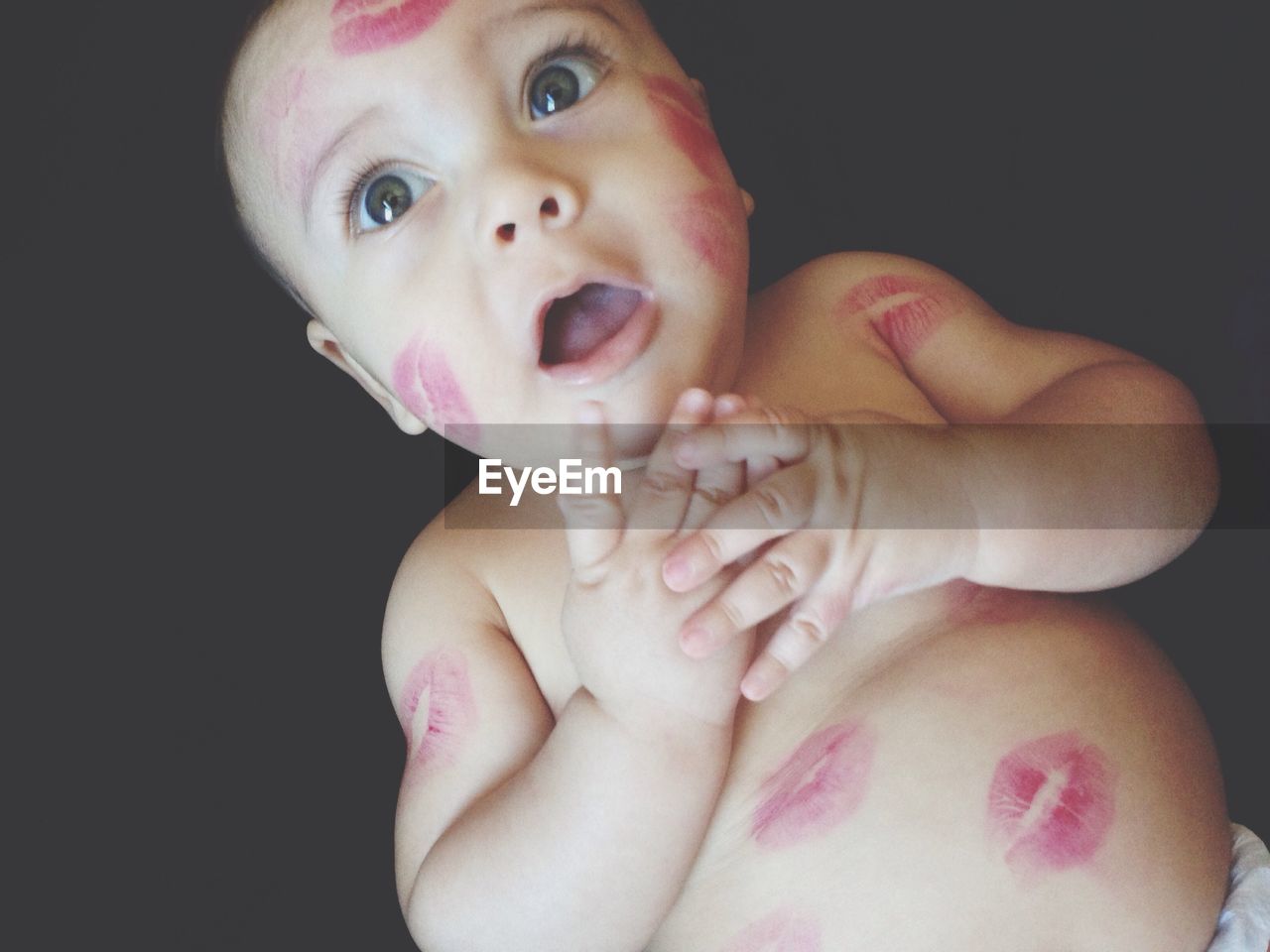 Directly above shot of shirtless baby with lipstick kisses lying against black background