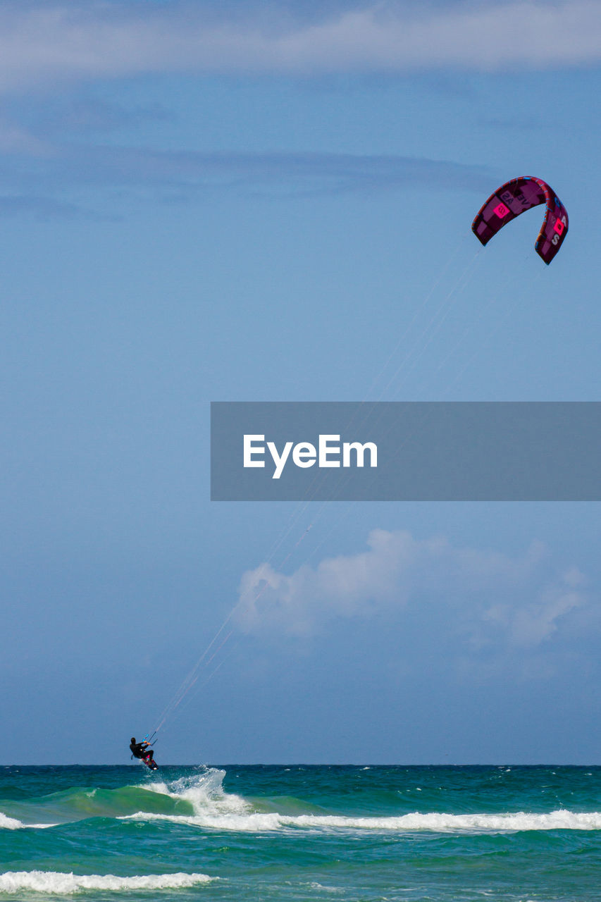 People in sea kite surfing against sky