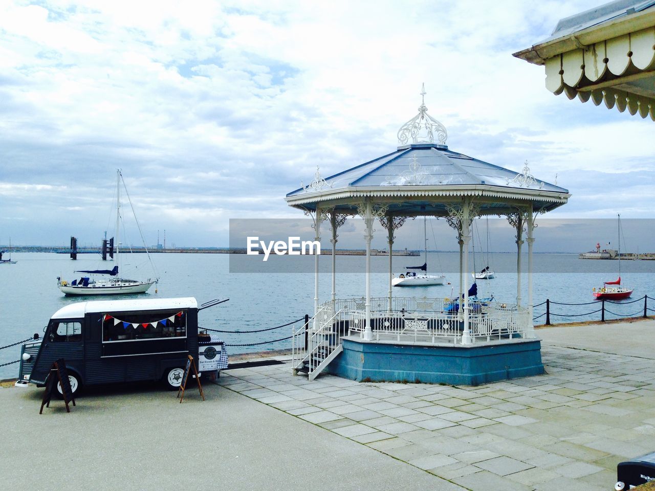 Van and gazebo at harbor against cloudy sky
